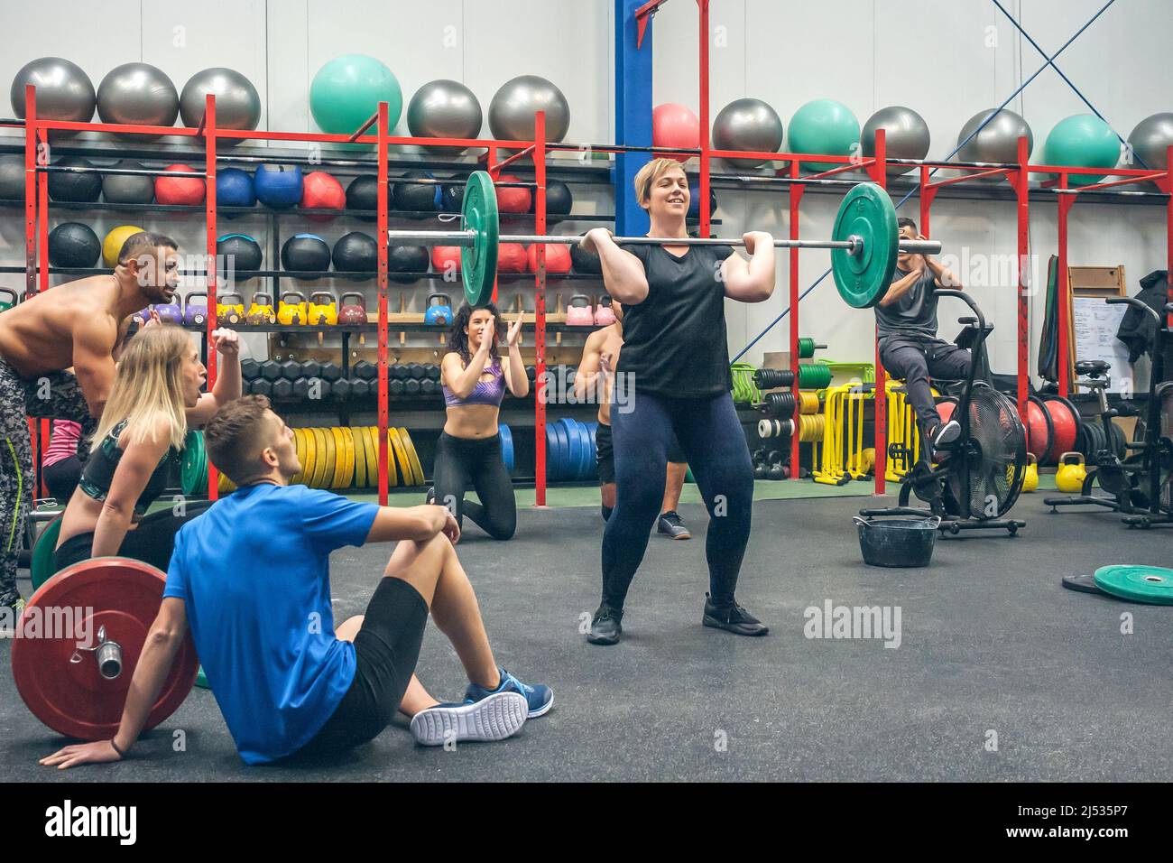 Stolze Frau, die Gewichte hebt, während ihre Kollegen im Fitnessstudio sie anfeuern Stockfoto