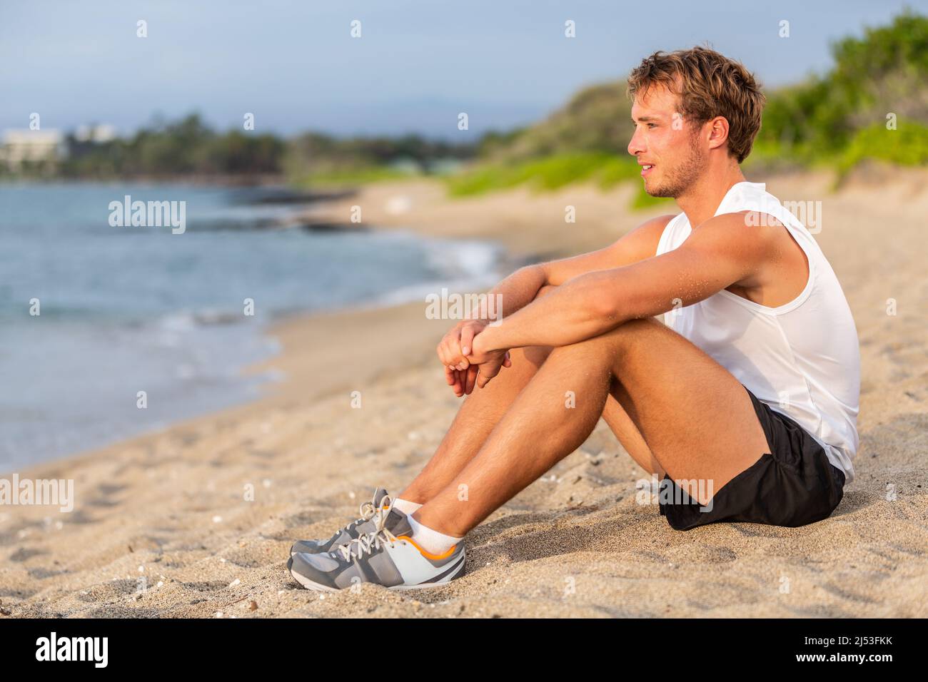 Fit junger Mann gesunde aktive Lebensweise Ruhe am Strand nach dem Training. Kaukasischer männlicher Athlet Portrait sitzen entspannend im Freien Stockfoto