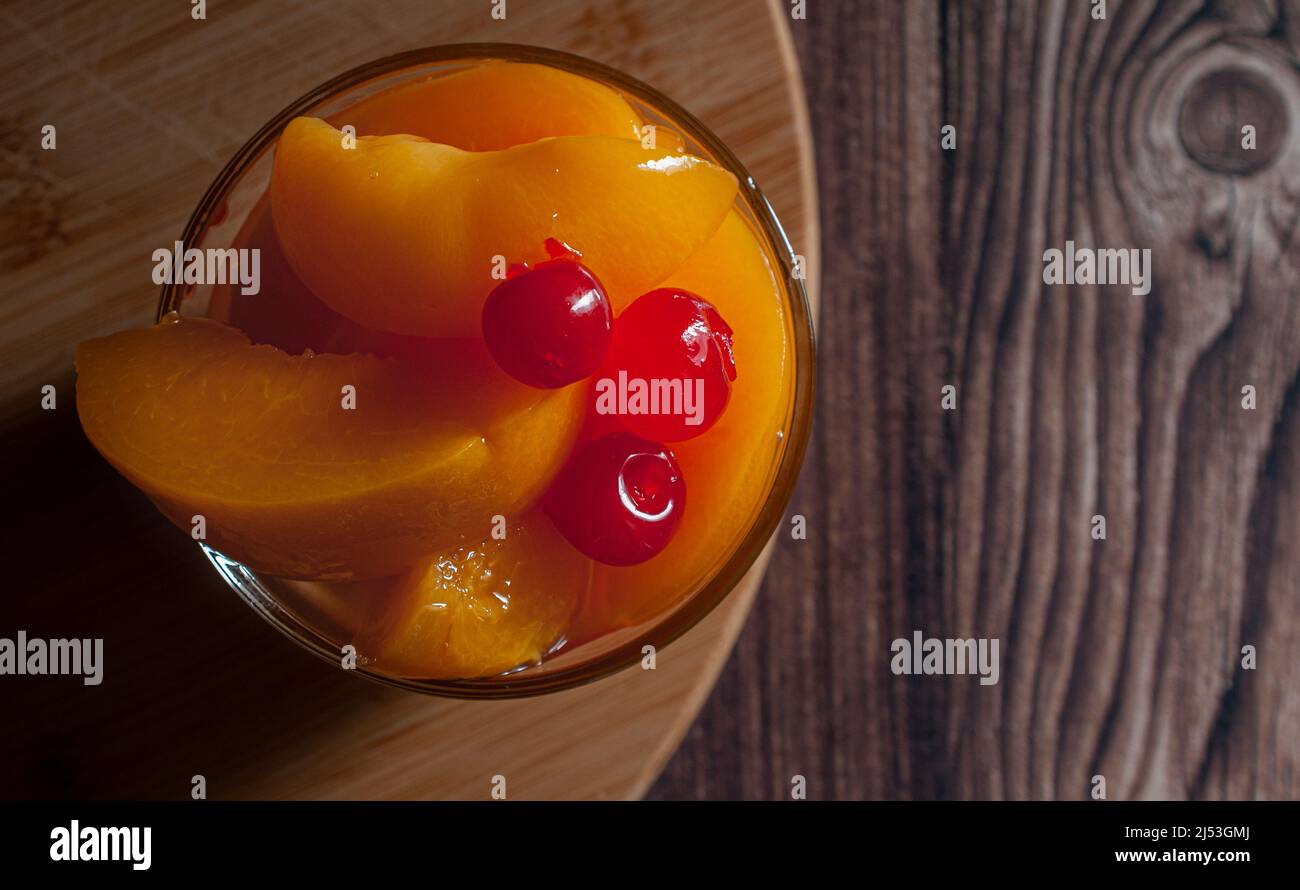In Sirup geschnittene Pfirsiche mit Kirschen auf einem Holzbrett. Stockfoto