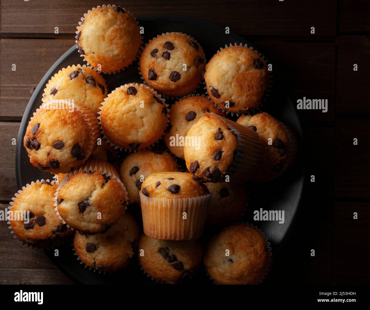 Chiaroscuro oder dunkle Makrofotografie, Vanille-Cupcakes mit Schokoladenstückchen auf einem schwarzen Teller, Konzept der hausgemachten Speisen Stockfoto
