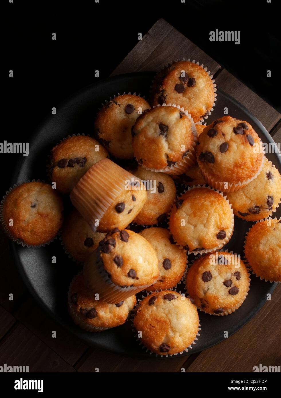 Chiaroscuro oder dunkle Makrofotografie, Vanille-Cupcakes mit Schokoladenstückchen auf einem schwarzen Teller, Konzept der hausgemachten Speisen Stockfoto