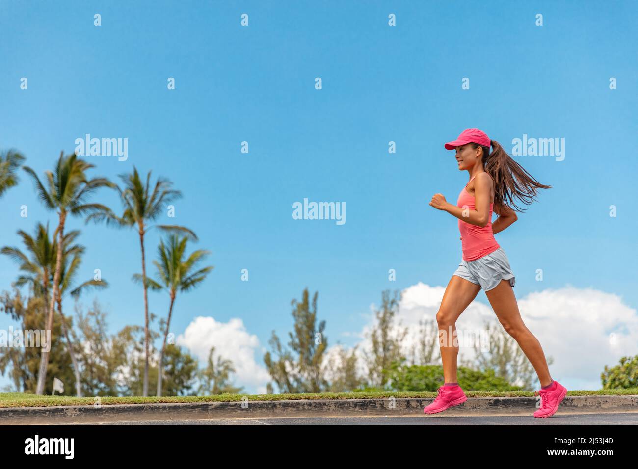 Happy Running Asian Girl Jogging im Park am Sommertag trägt rosa Kappe für Sonnenschutz. Läuferin Frau, die auf dem Bürgersteig Kardio trainiert. Profil voll Stockfoto