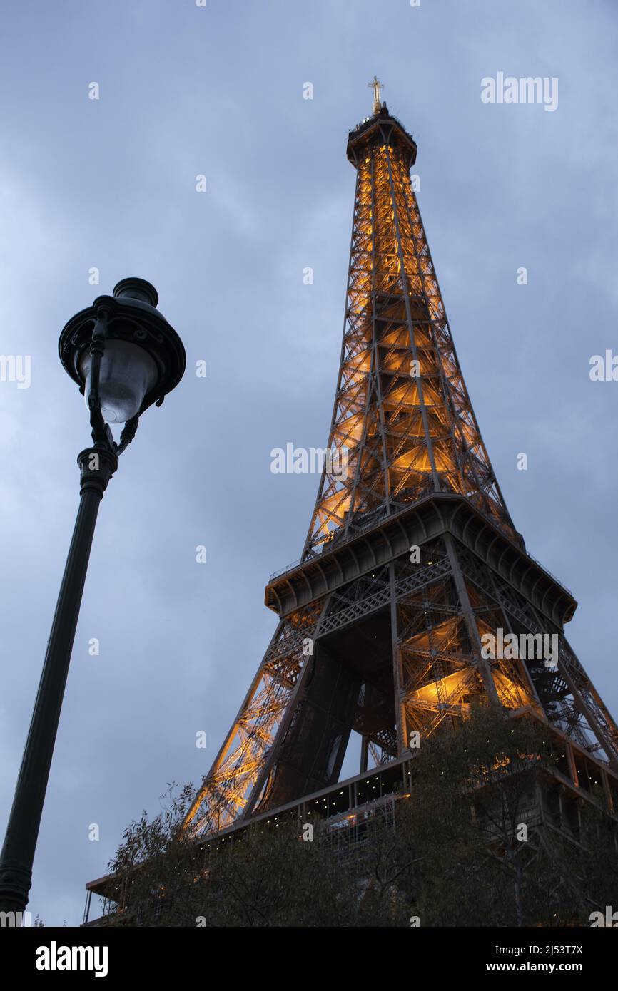Paris, Frankreich: Eine Straßenlaterne und der Eiffelturm, Metallturm, fertiggestellt 1889 für die Weltausstellung, beleuchtet an einem bewölkten Abend Stockfoto