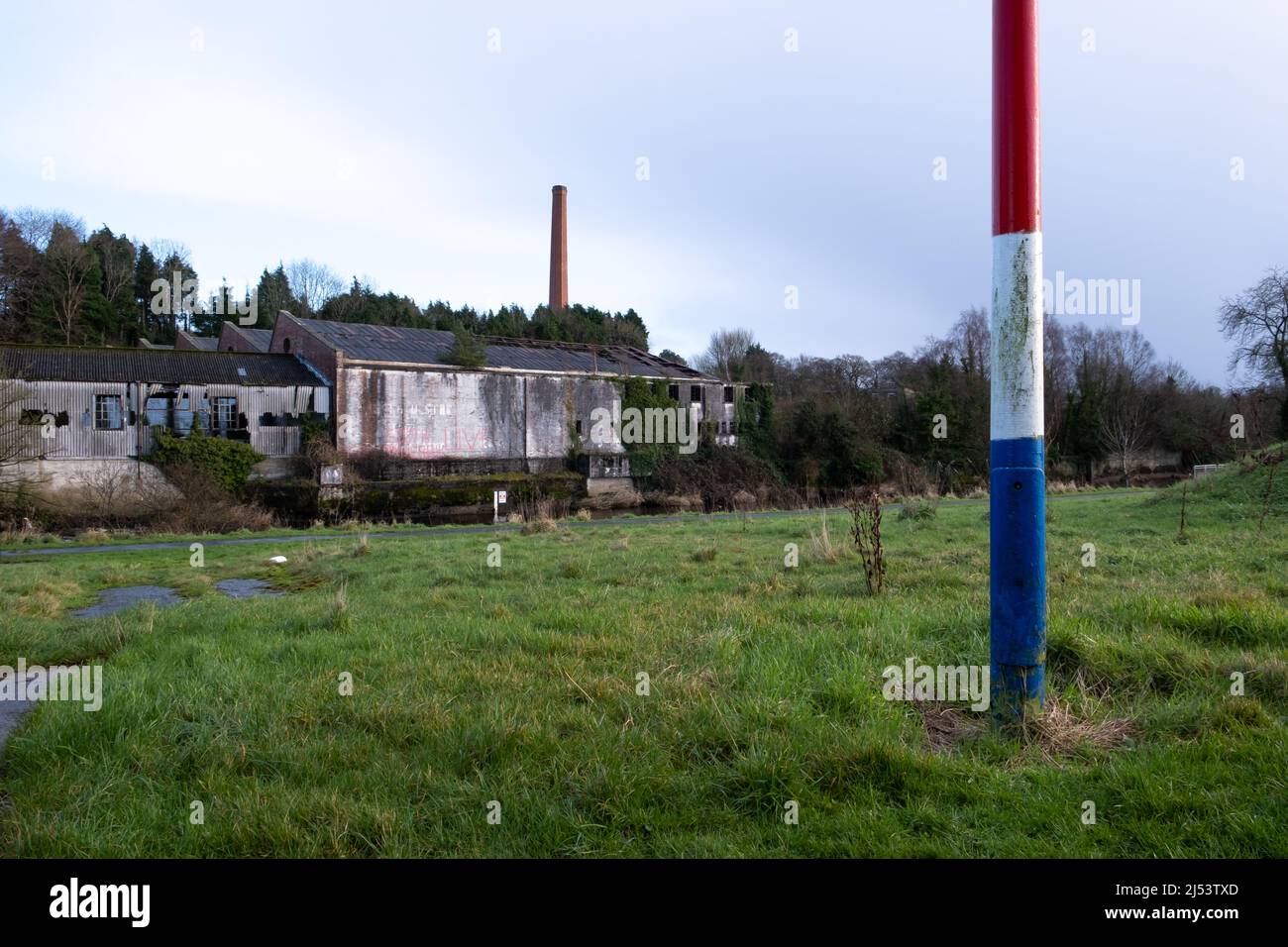 Rot weiß und blau bemalter Telegrafenmast und Blick auf den alten Kamin in der verfallenen Old Bleach Leinenfabrik in Randalstown County Antrim. Stockfoto
