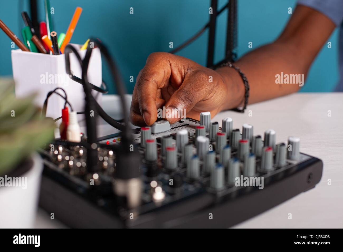 Nahaufnahme der Content Creator Hand Anpassung Master Volume Fader auf Mischpult auf dem Schreibtisch während Live-Podcast. Vlogger arbeitet an den Toneinstellungen des Equalizers, der für die Übertragung von Live-Streams verwendet wird. Stockfoto
