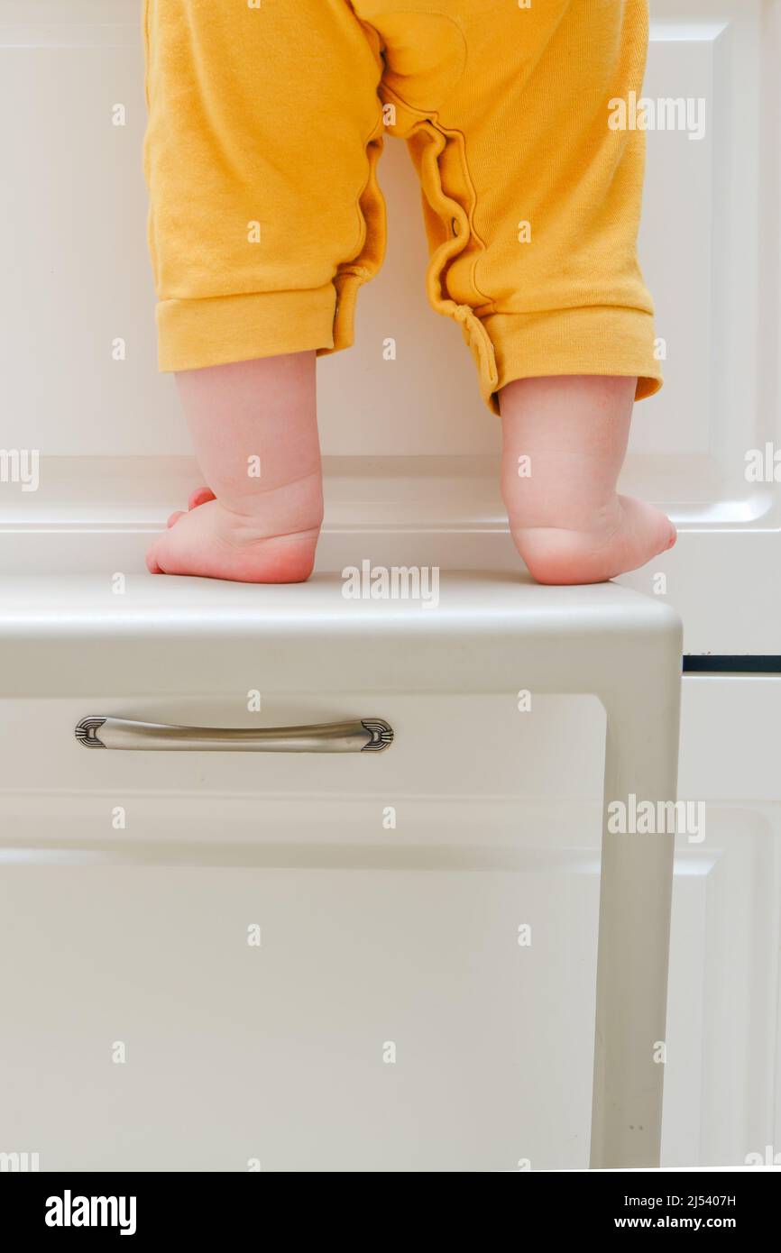 Kleinkind Baby Junge kletterte mit seinen Füßen auf einem Hochstuhl auf den Küchenschrank klettern. Probleme mit der Kindersicherheit im heimischen Zimmer, kleines Kind Stockfoto