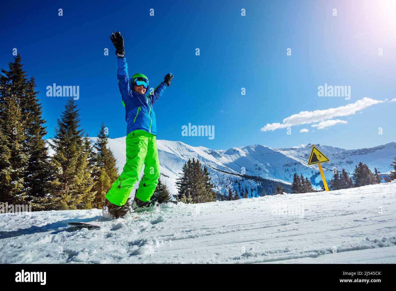 Boy auf Snowboard in Helm und Maske heben die Hände nach oben Stockfoto