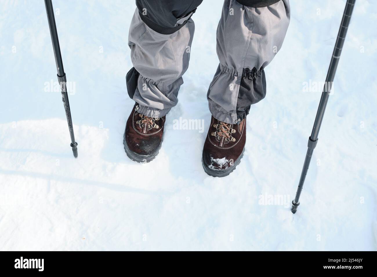 Aufnahme eines nicht erkennbaren Reisenden in bequemer Kleidung und Stiefel, der am Wintertag mit Trekkingstöcken wanderte Stockfoto
