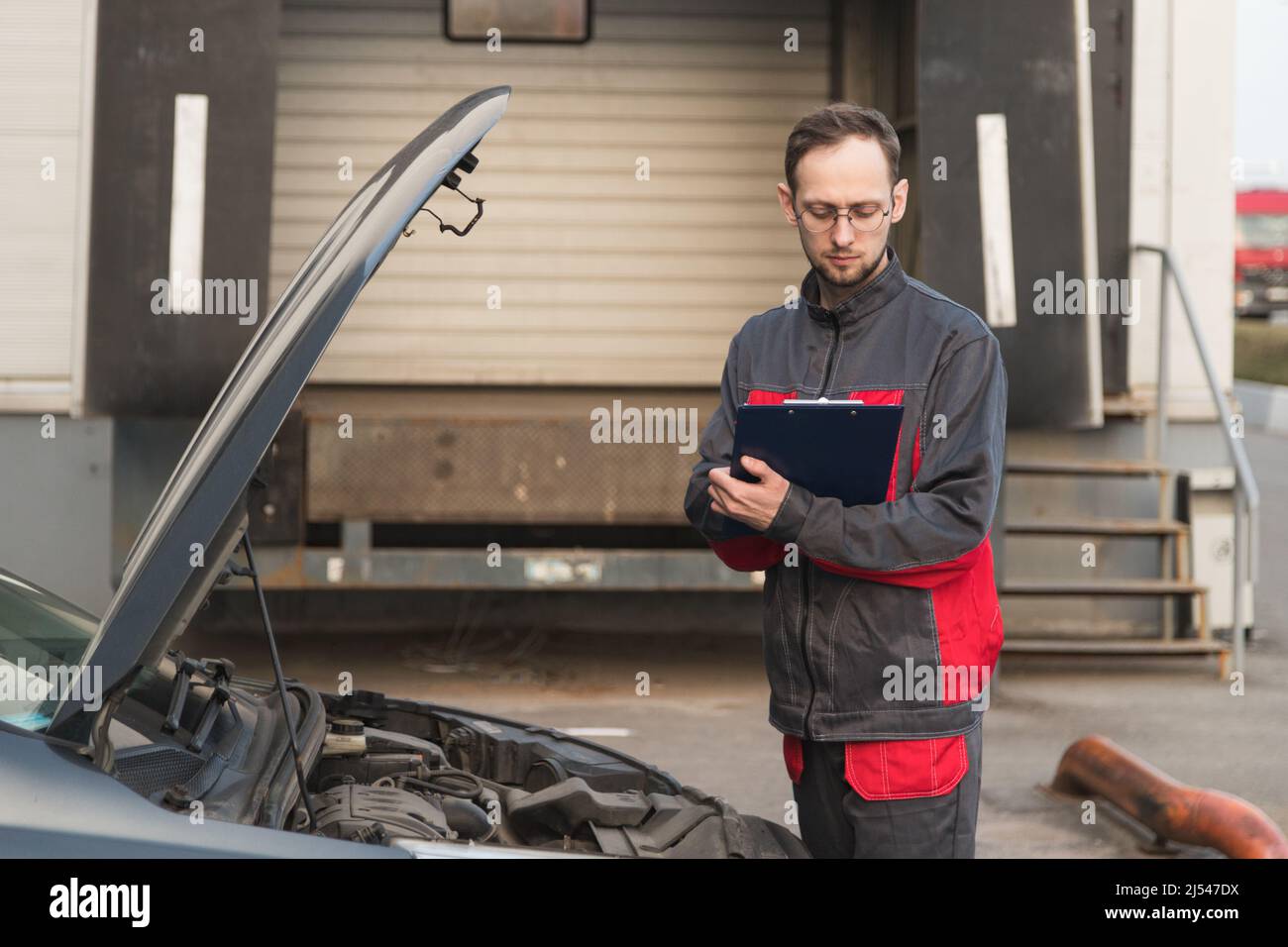 Kaukasischer Mechaniker in Uniform, die Liste der Fehlfunktionen an der Kfz-Reparaturstation macht. Autowartung Stockfoto