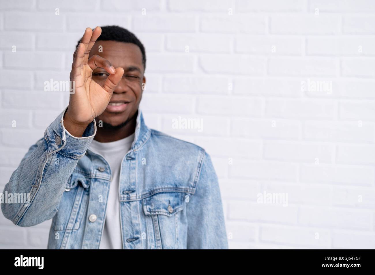Portrait junger hübscher afrikanischer schwarzer Mann, der eine gute Geste in Jeans-Jacke gegen Backstein zeigt, mit einer Wand im Freien mit Copyspace. Stockfoto