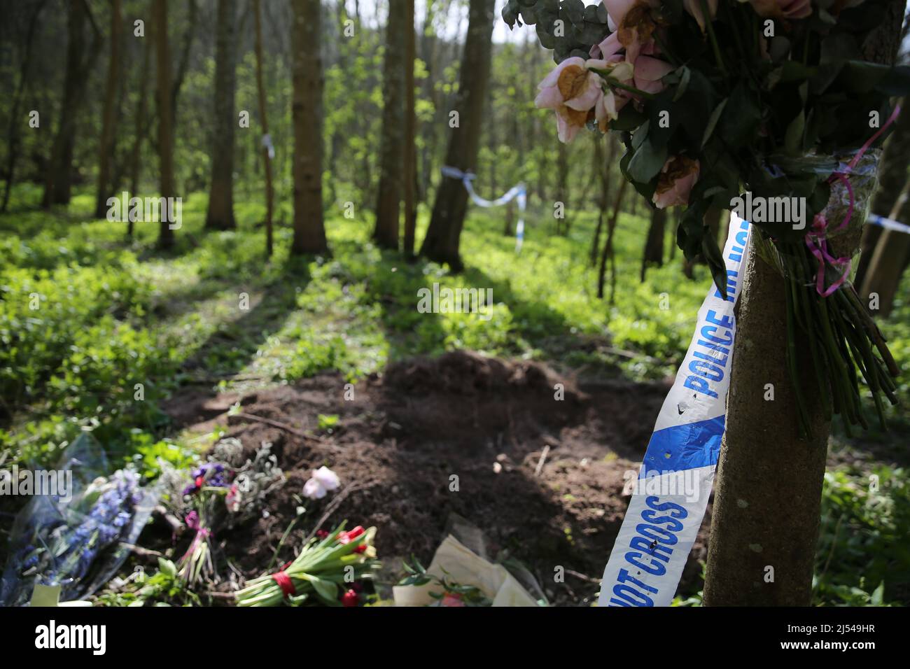 Flaches Grab in Wäldern mit Blumen und Polizeiband - Wiederaufbau Stockfoto