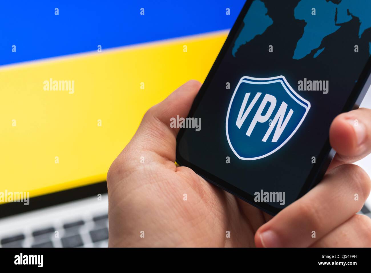 VPN in der Ukraine. Sicheres und sicheres Internet-Konzept. Datenschutz. Hand mit Mobiltelefon und VPN-Anwendung. Flagge und Laptop auf dem Hintergrundbild Stockfoto