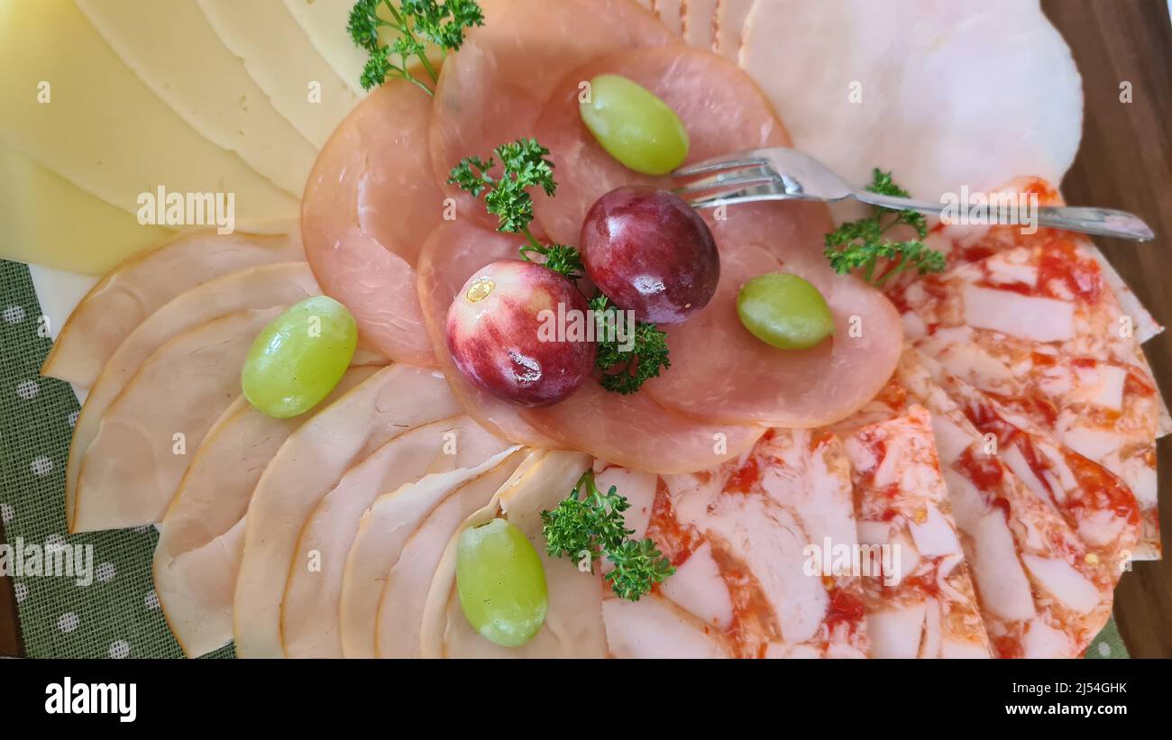Food-Tablett mit leckeren Salami, Schinkenstücken, Wurst, Tomaten, Salat und Gemüse - Fleischplatte mit Auswahl - Wurst und Wurst geschnitten auf einem Stockfoto
