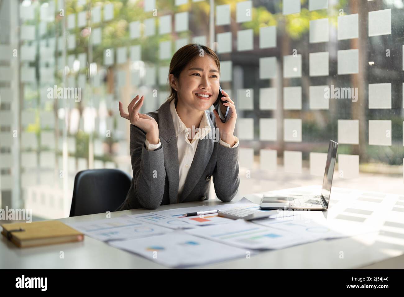 Lächelnde asiatische Frau im Gespräch Berater auf Handy im modernen Büro Stockfoto