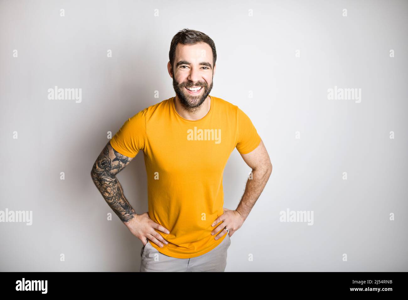 Porträt eines lässigen jungen Mannes mit Bart und Tattoo und gebranntem Orange-Hemd auf weißem Hintergrund Stockfoto
