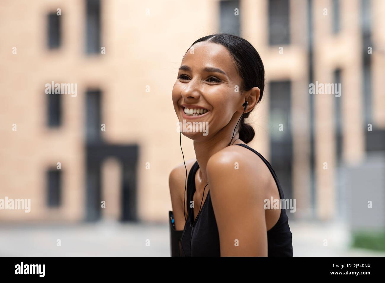 Lächelnde junge arabische Frau Athlet Brünette in Kopfhörern genießt Lieblingsmusik online im Training Stockfoto