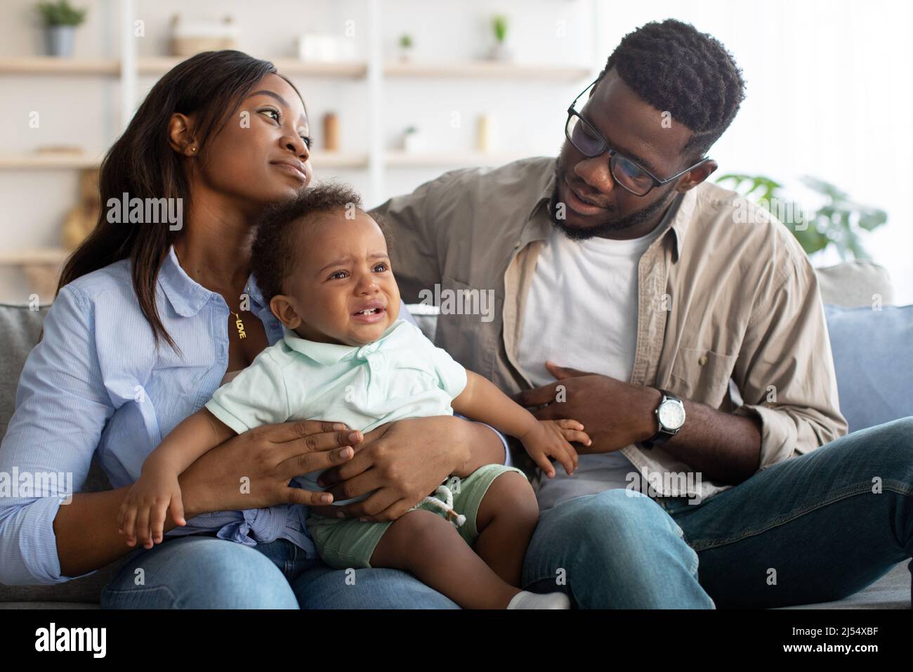 Afroamerikanische Eltern trösten weinendes Kind auf dem Sofa Stockfoto