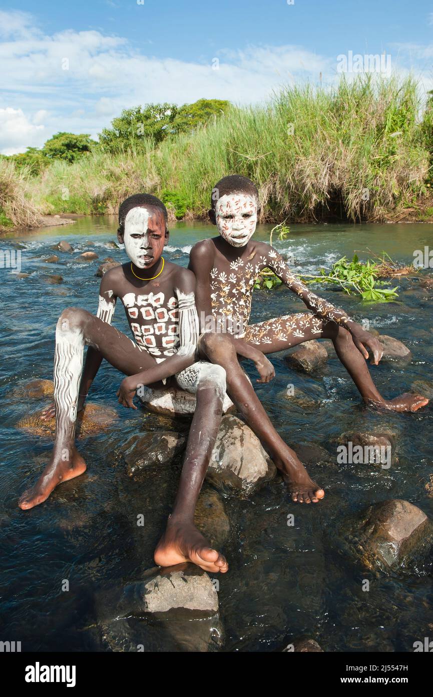 Zwei Surma jungen mit Körper Gemälde sitzt auf einem Felsen im Fluss