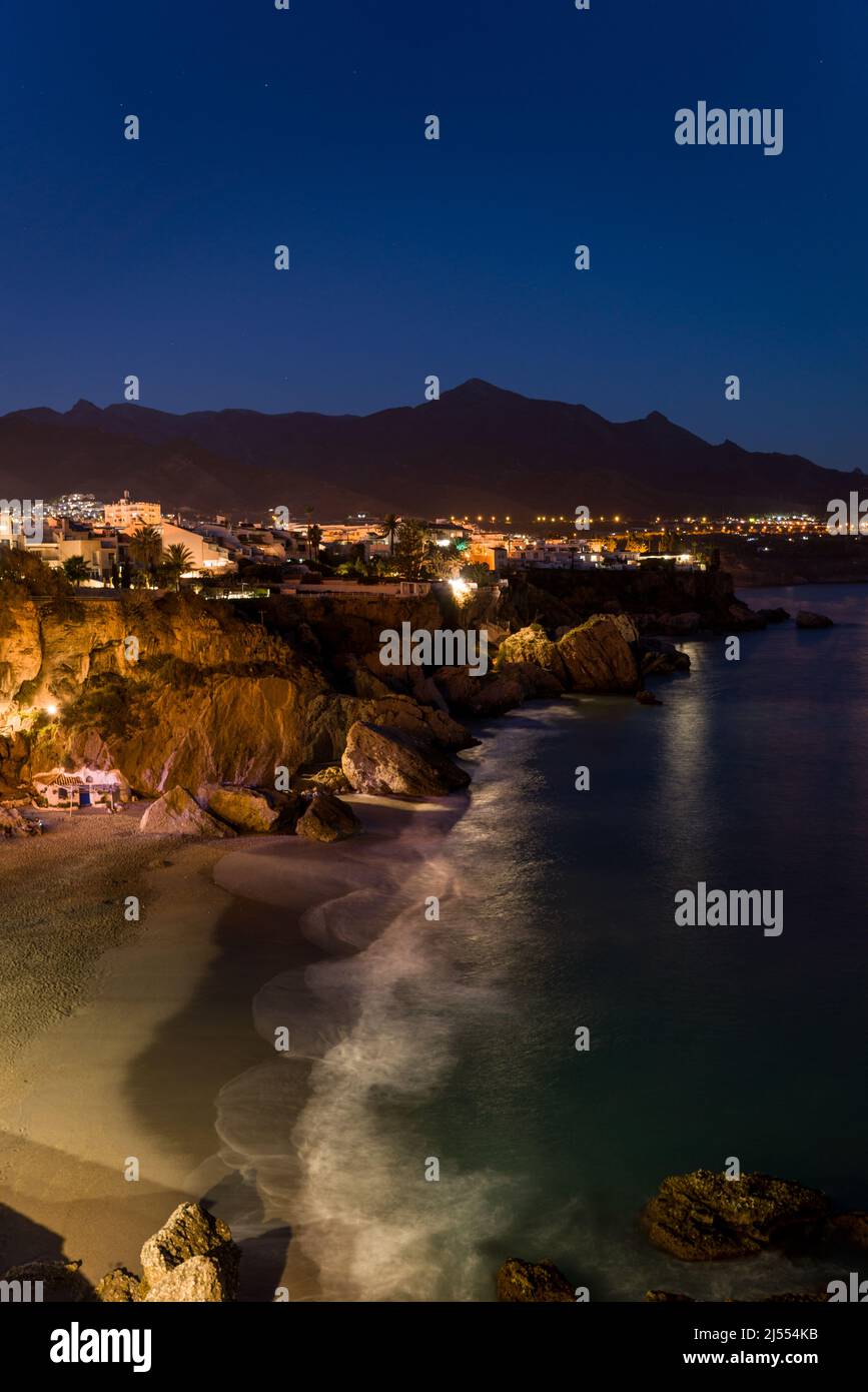 Fotografie mit Langzeitbelichtung der schönen Stadt Nerja, Spanien bei Nacht. Blick auf die Küste mit beleuchteten Häusern. Im Hintergrund Sierra Nevada Stockfoto