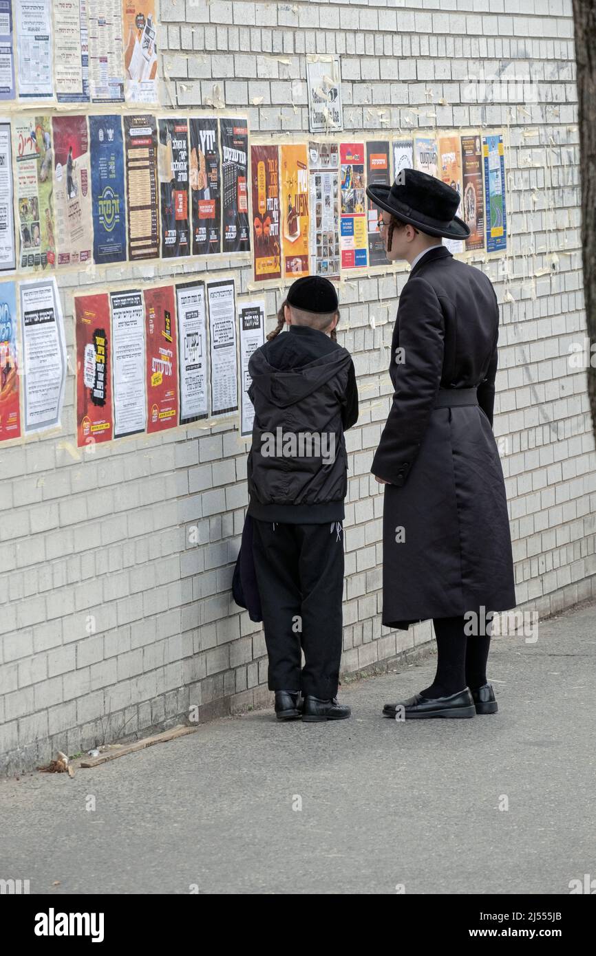 Während des Passahfestes halten chassidische Brüder an, um Poster zu lesen, die hauptsächlich auf Jiddisch mit etwas Hebräisch sind. In Williamsburg, Brooklyn, New York City. Stockfoto