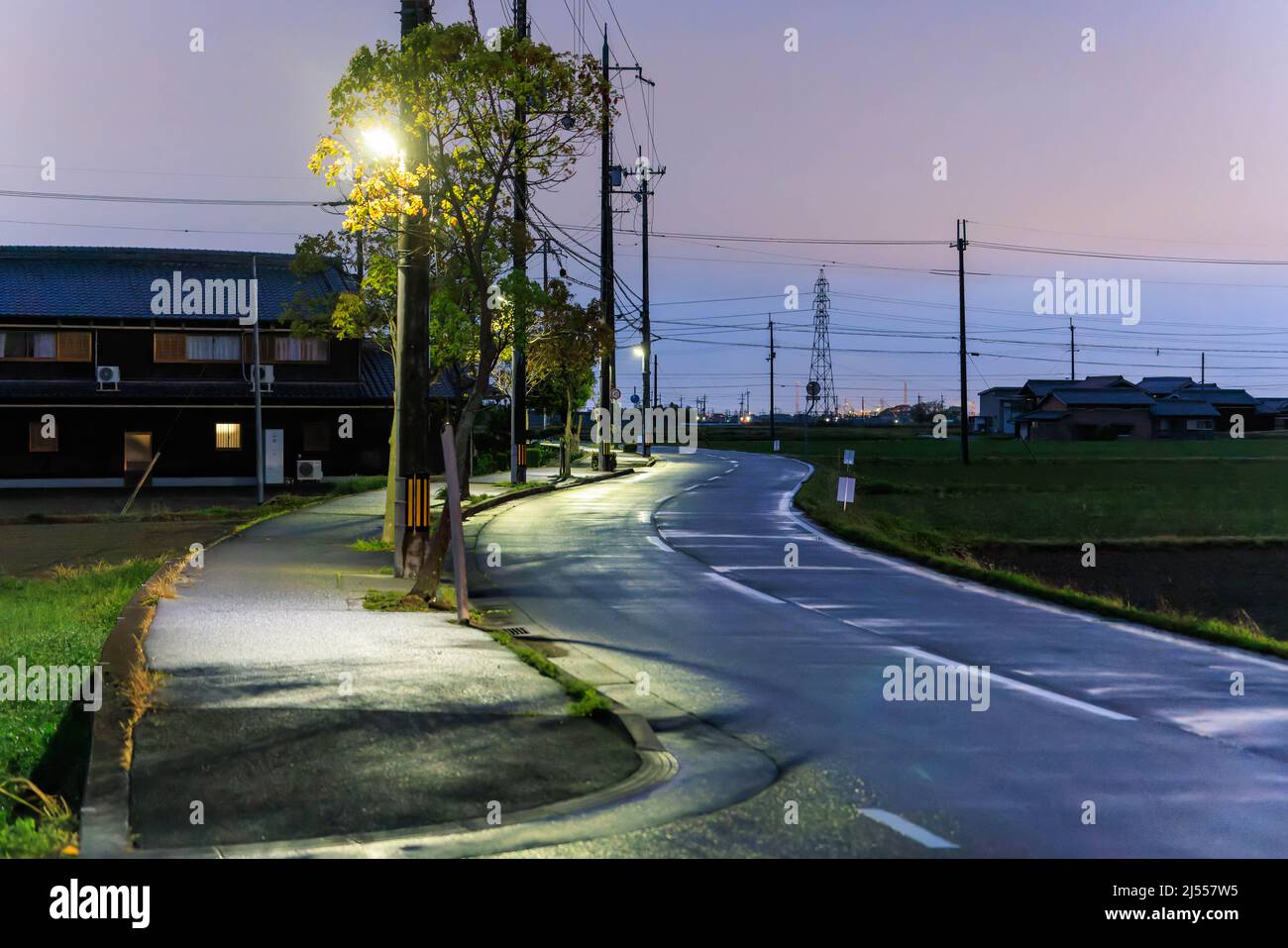 Nasse kurvenreiche Straße durch ländliche Gebiete bei Sonnenuntergang nach Regen Stockfoto