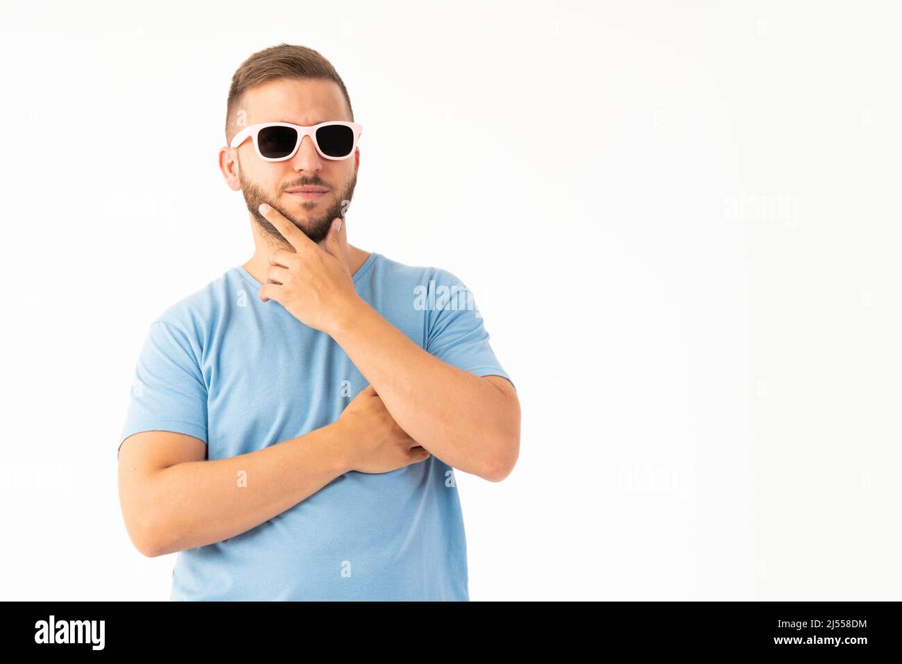 Ein junger Mann, der mit einer Sonnenbrille auf weißem Hintergrund denkt Stockfoto