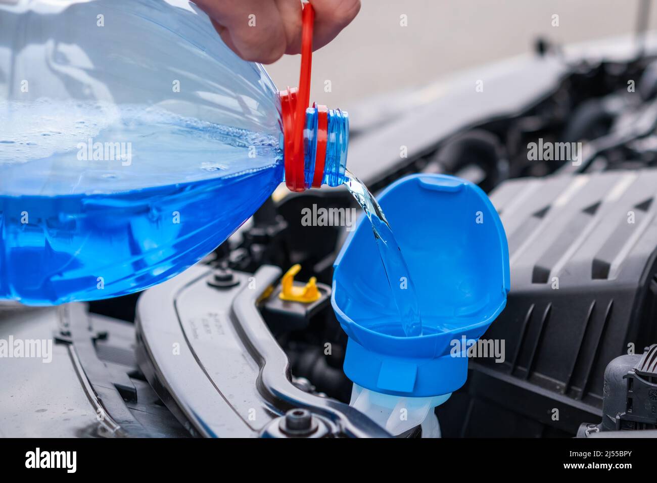 Nahaufnahme des Fahrers, der blaue, nicht gefrierende Scheibenwaschflüssigkeit in den Tank des Fahrzeugs gießt. Stockfoto