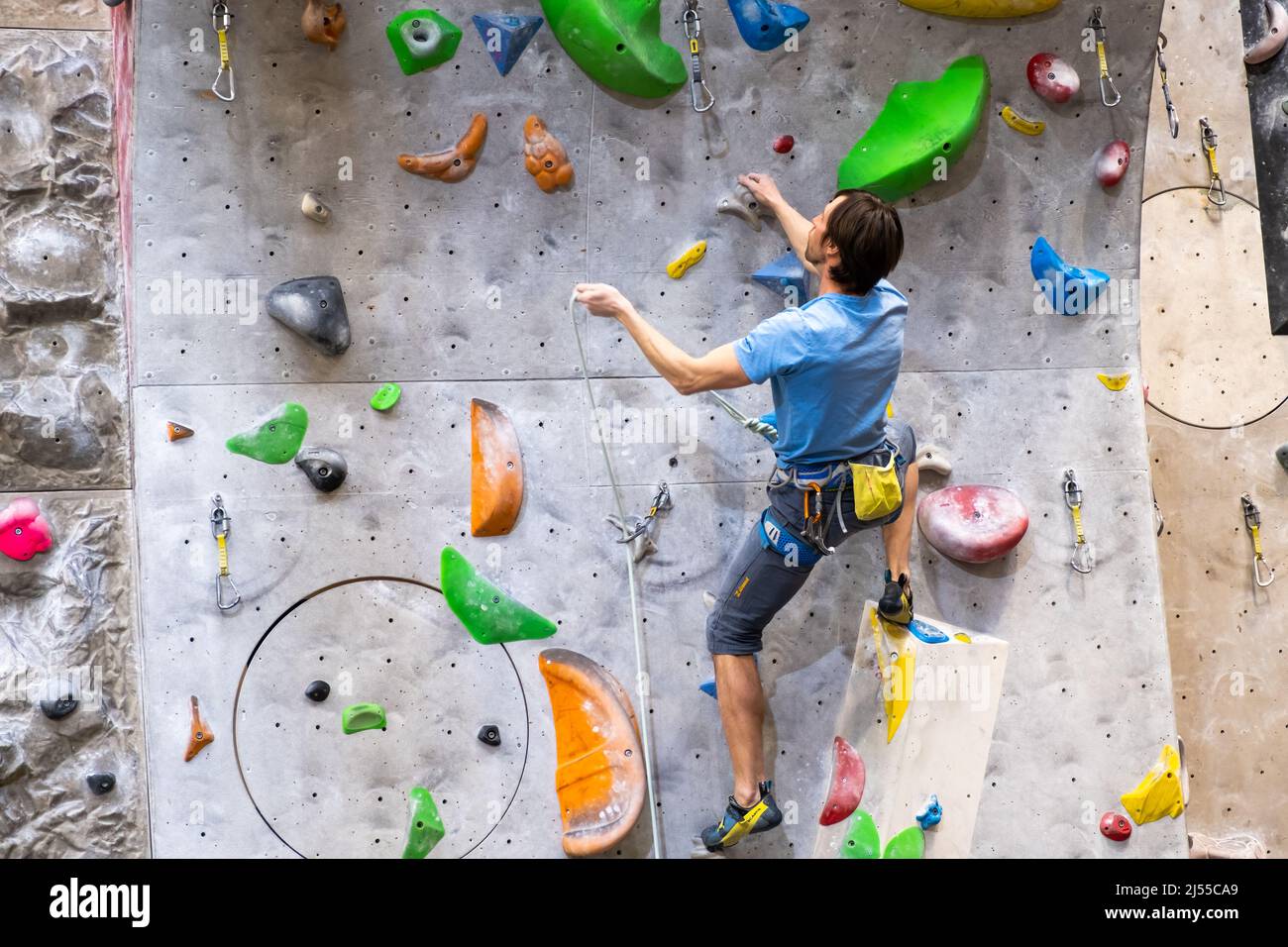 Der Kletterer trainiert an der künstlichen Felswand mit Versicherung in der Boulderhalle, April 2022, Prag, Tschechische Republik. Stockfoto
