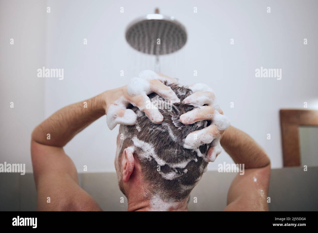 Rückansicht des Mannes beim Waschen der Haare in der Dusche im Badezimmer. Nasse Haare mit Schaum von Shampoo. Stockfoto