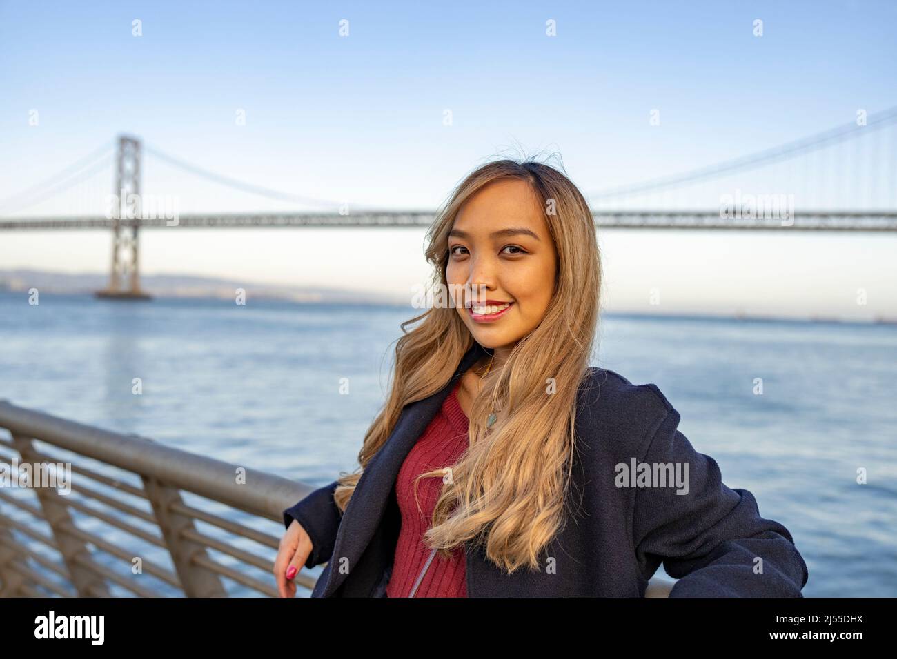 Junge Asiatin mit der Oakland Bay Bridge und der San Francisco Bay im Hintergrund Stockfoto