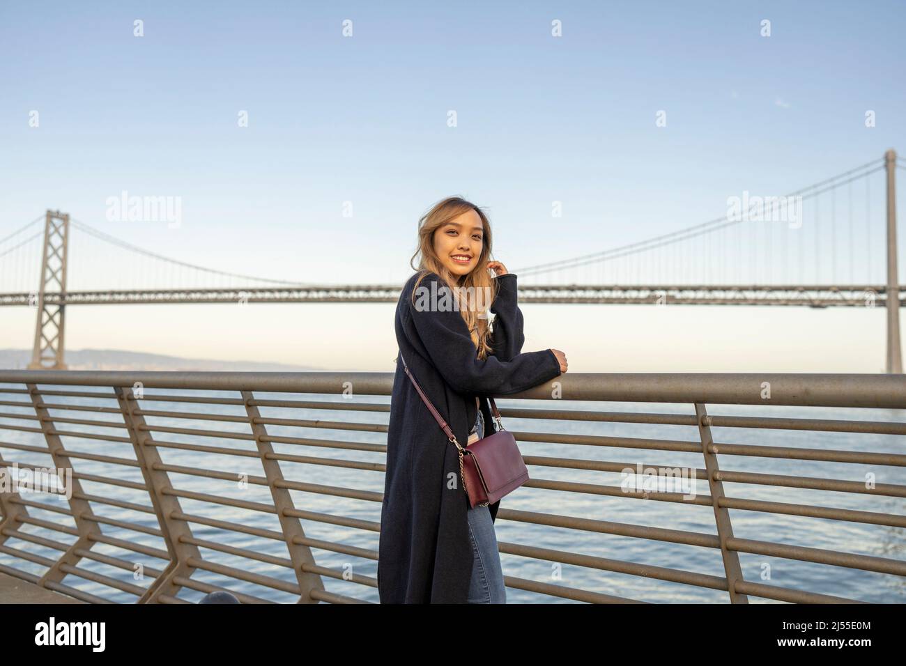 Am späten Nachmittag wurden Halbkörperportraits einer jungen Frau mit der Oakland Bay Bridge und der San Francisco Bay im Hintergrund | Lifestyle Travel in the City Stockfoto