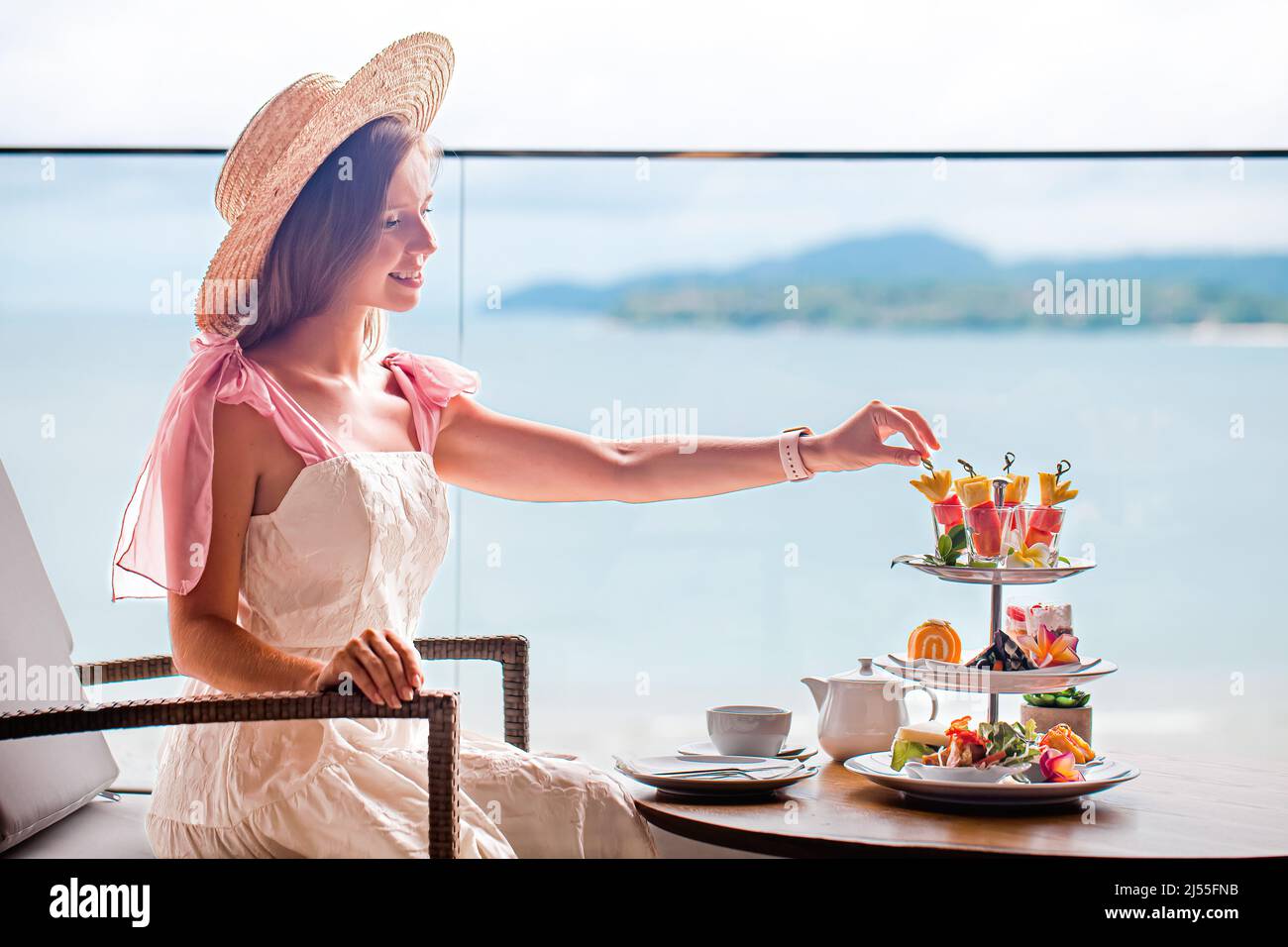 Junge Dame in weißem Kleid trinkt Tee am Nachmittagstee mit verschiedenen Süßigkeiten Stockfoto