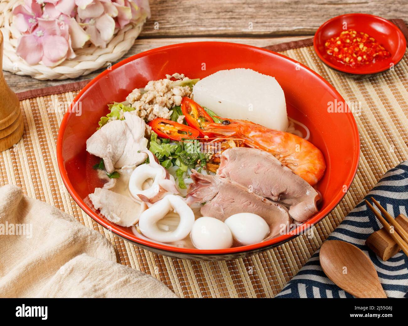 Verschiedene Nudeln Suppe mit Garnelen, Trupp und Gemüse in einer Schüssel mit Löffel und Essstäbchen isoliert auf Matte Seitenansicht auf Holztisch taiwan Essen Stockfoto