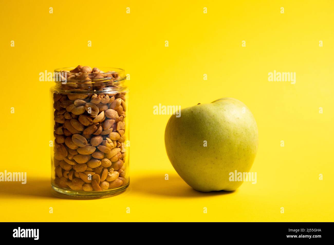 Erdnüsse im Glas und grüner Apfel auf gelbem Hintergrund Stockfoto