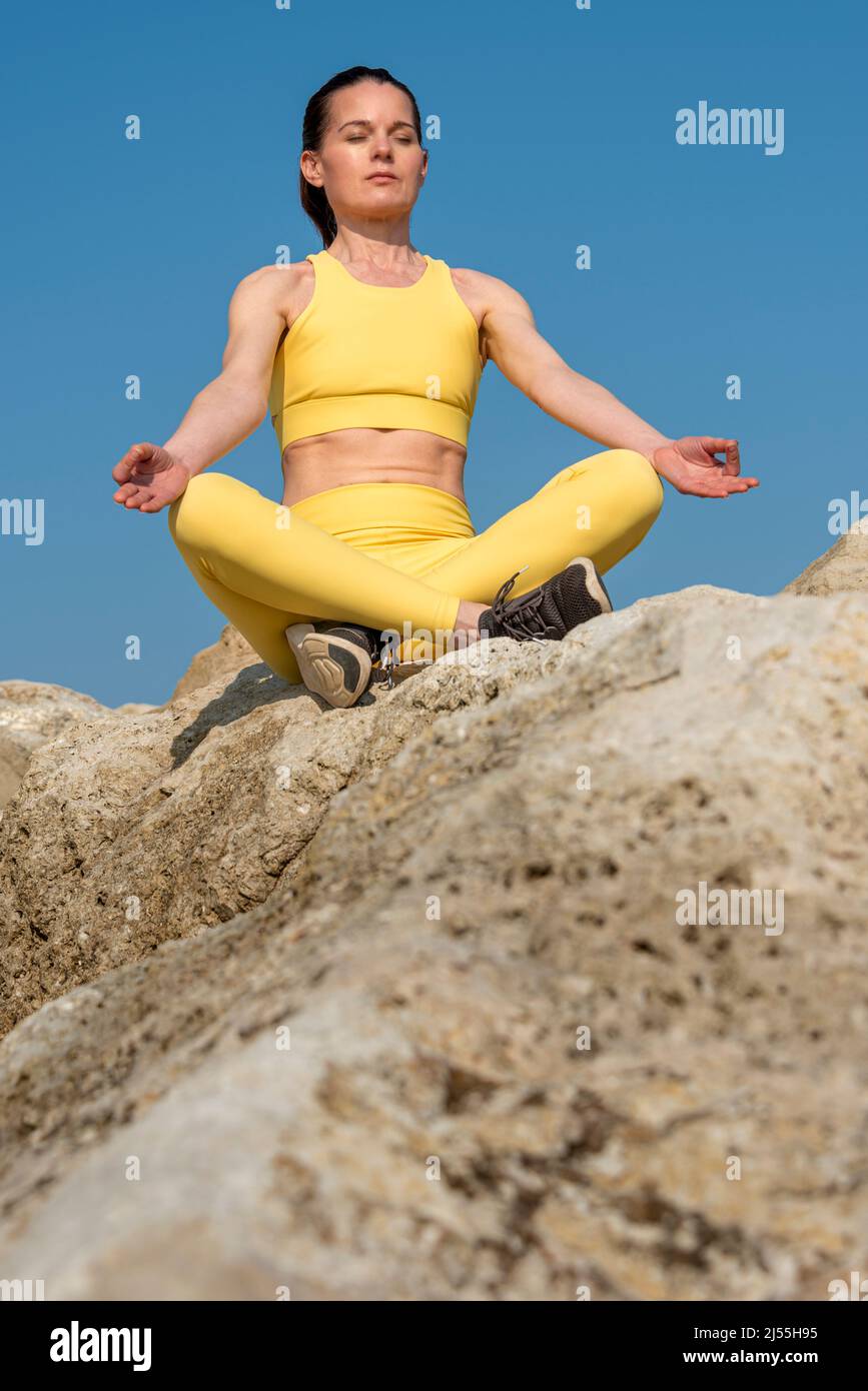 Frau, die auf Felsen sitzt, meditiert und praktiziert Yoga im Freien in der Sonne. Stockfoto