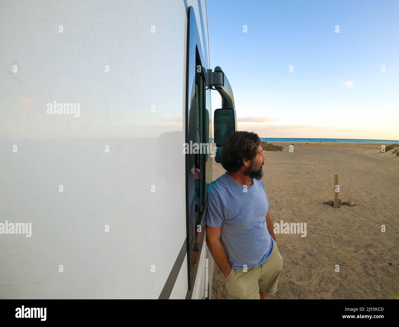 Reifer Mann steht vor einem modernen Wohnmobil bewundern das Meer und genießen den Strand. Travel people Lifestyle-Konzept. Campingplatz der Freiheit. Erwachsene l Stockfoto