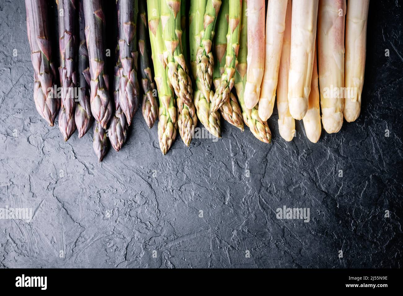 Grüne, violette und weiße Spargelsprossen auf schwarzem Brett Draufsicht flach liegend. Food-Fotografie Stockfoto