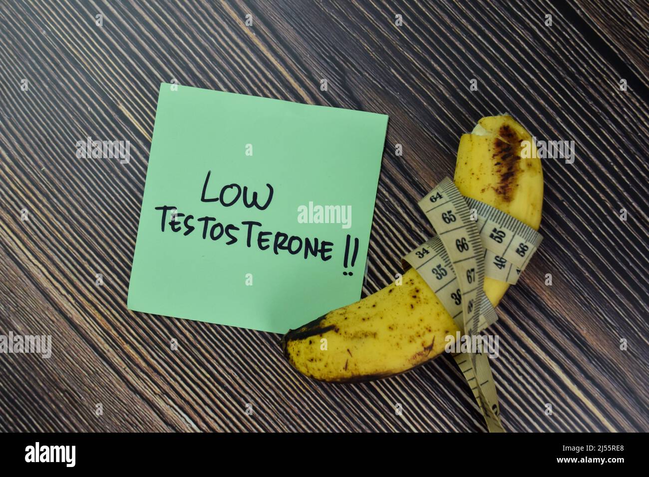 Low Testoterone schreiben auf Haftnotizen und Banane isoliert auf Holztisch. Stockfoto