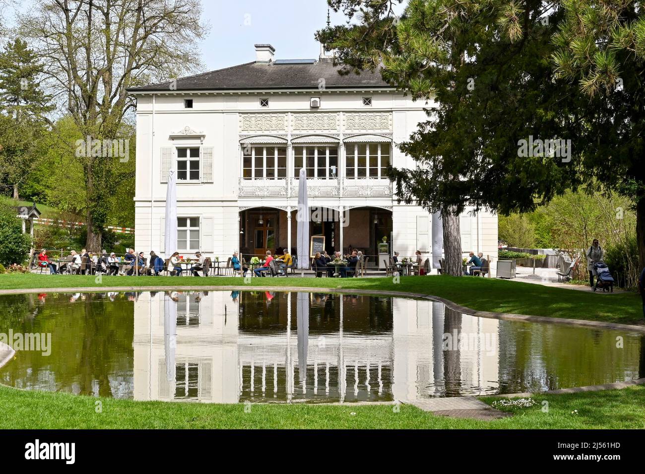 Basel, Schweiz - April 2022: Menschen im Café auf der Rückseite der Villa Merian im Merian-Garten, einem botanischen Garten in der Nähe des Stadtzentrums Stockfoto