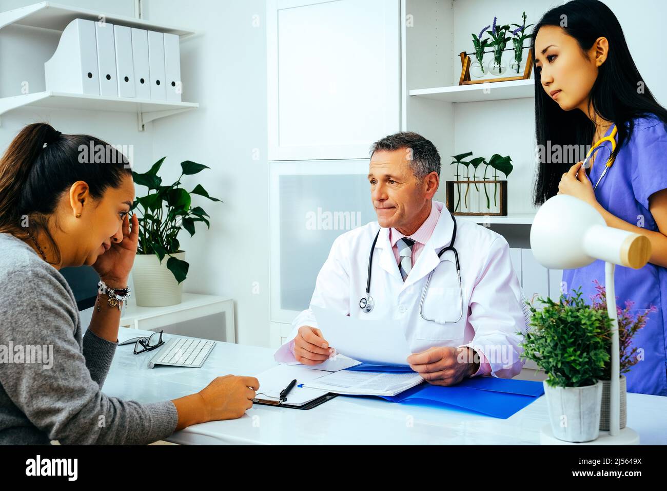 Ärztin und Krankenschwester im Gespräch mit einer traurigen, besorgten Patientin in der Bürogesundheitsbranche Stockfoto