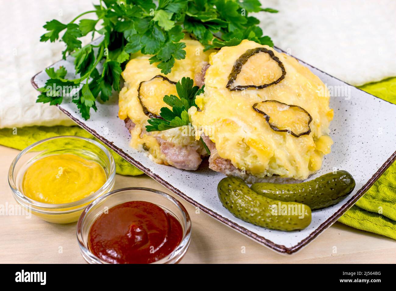 Hausgemachtes Schweinefleischschnitzel mit Käse und Gemüse, verschiedene Saucen und eingelegte Gurken zum Abendessen auf dem Tisch in der Küche. Stockfoto
