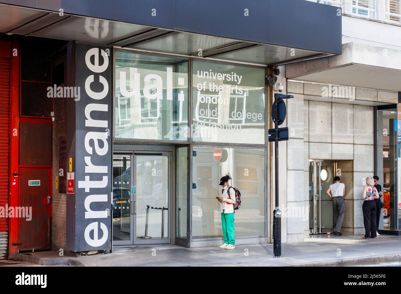 Ein Student wartet vor dem Eingang von UAL: London College of Fashion in der John Prince's Street, in der Oxford Street, London, Großbritannien Stockfoto