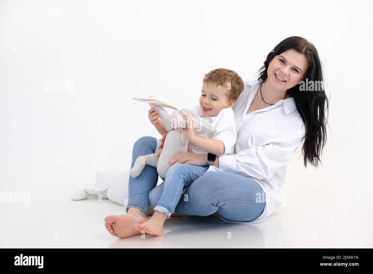 Porträt einer fröhlichen Frau, die mit einem kleinen Jungen spielt, ein weiches Spielzeug-Kaninchen hält und auf dem Boden sitzt. Gemeinsam spielen. Speicherplatz kopieren Stockfoto