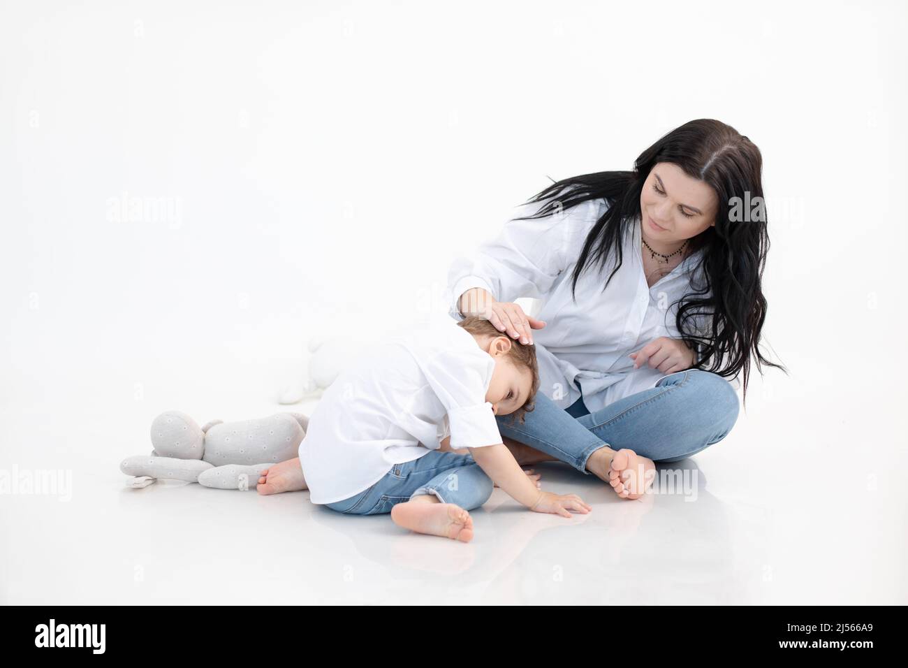 Frau und Junge sitzen zusammen auf dem Boden, weißer Hintergrund. Umarmen, Mutter kümmern. Autismus-Spektrum-Störung. Psychische Gesundheit Stockfoto