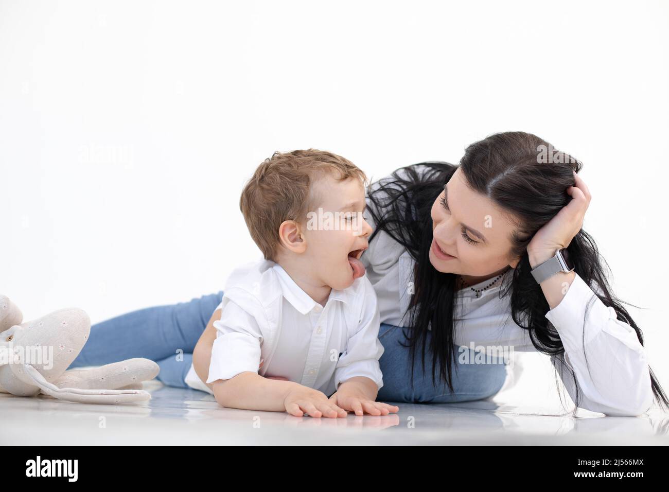 Die schwarzhaarige Lehrerin und der kleine Junge zeigen die Zunge und liegen auf dem Boden. Logopädie, Frühentwicklung, Logopädie Stockfoto