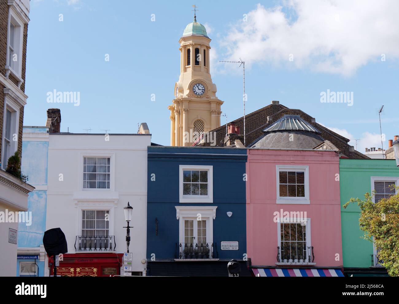 London, Greater London, England, April 09 2022: Farbenfrohe Immobilien an der Portabello Road in Notting Hill mit dem Glockenturm der St. Peters Kirche dahinter Stockfoto