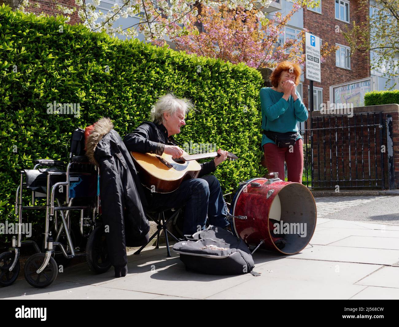Elderly Mann und Frauen mit einem Rollstuhl busking auf Portabello Road, spielen Gitarre, Schlagzeug und Mundharmonika. London. Stockfoto