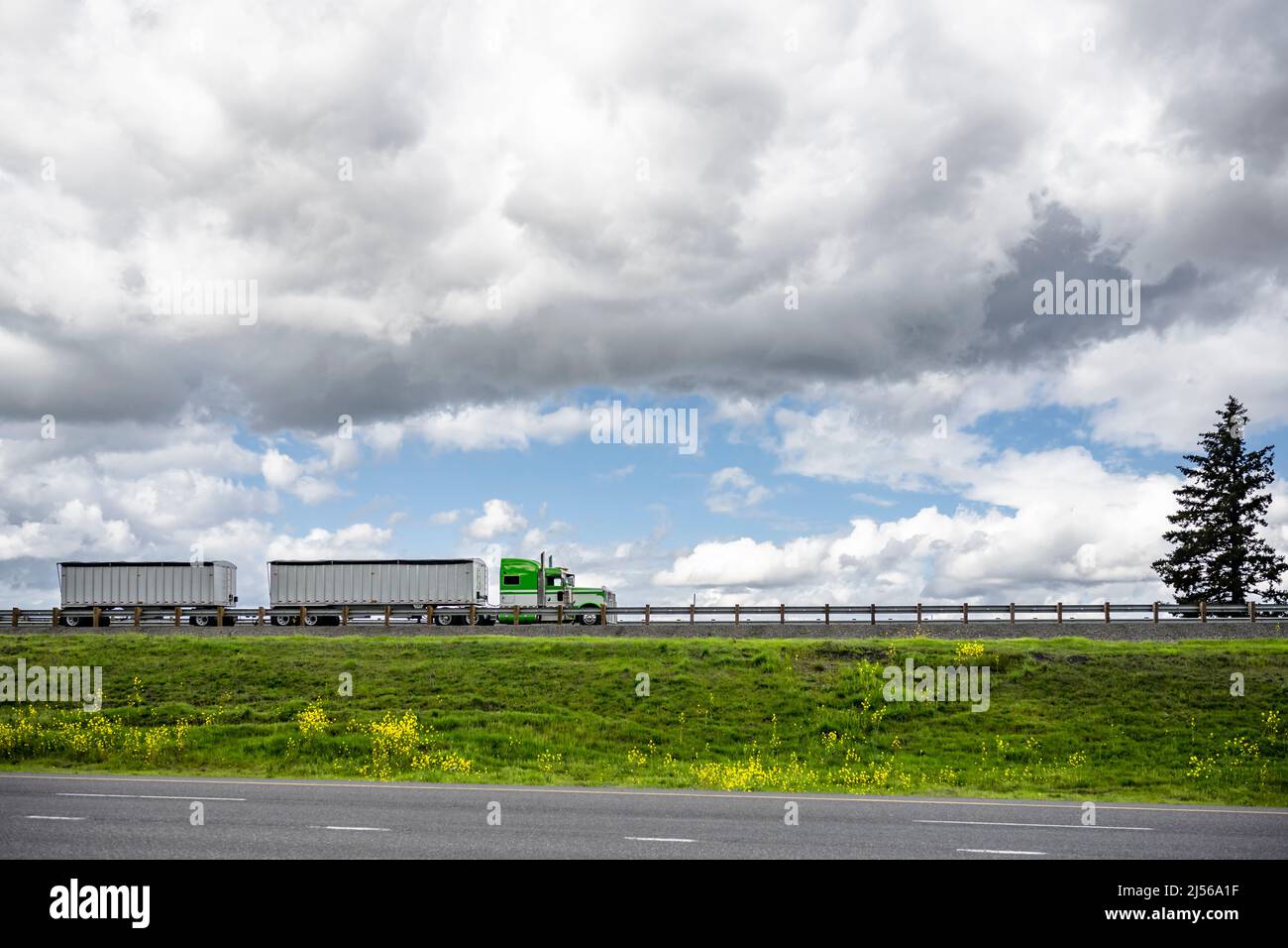 Industrielle leistungsstarke klassische Motorhaube American Green Big Rig Sattelschlepper mit zwei beladenen Bulk-Sattelanhänger Transport von Fracht auf der Straße Stockfoto