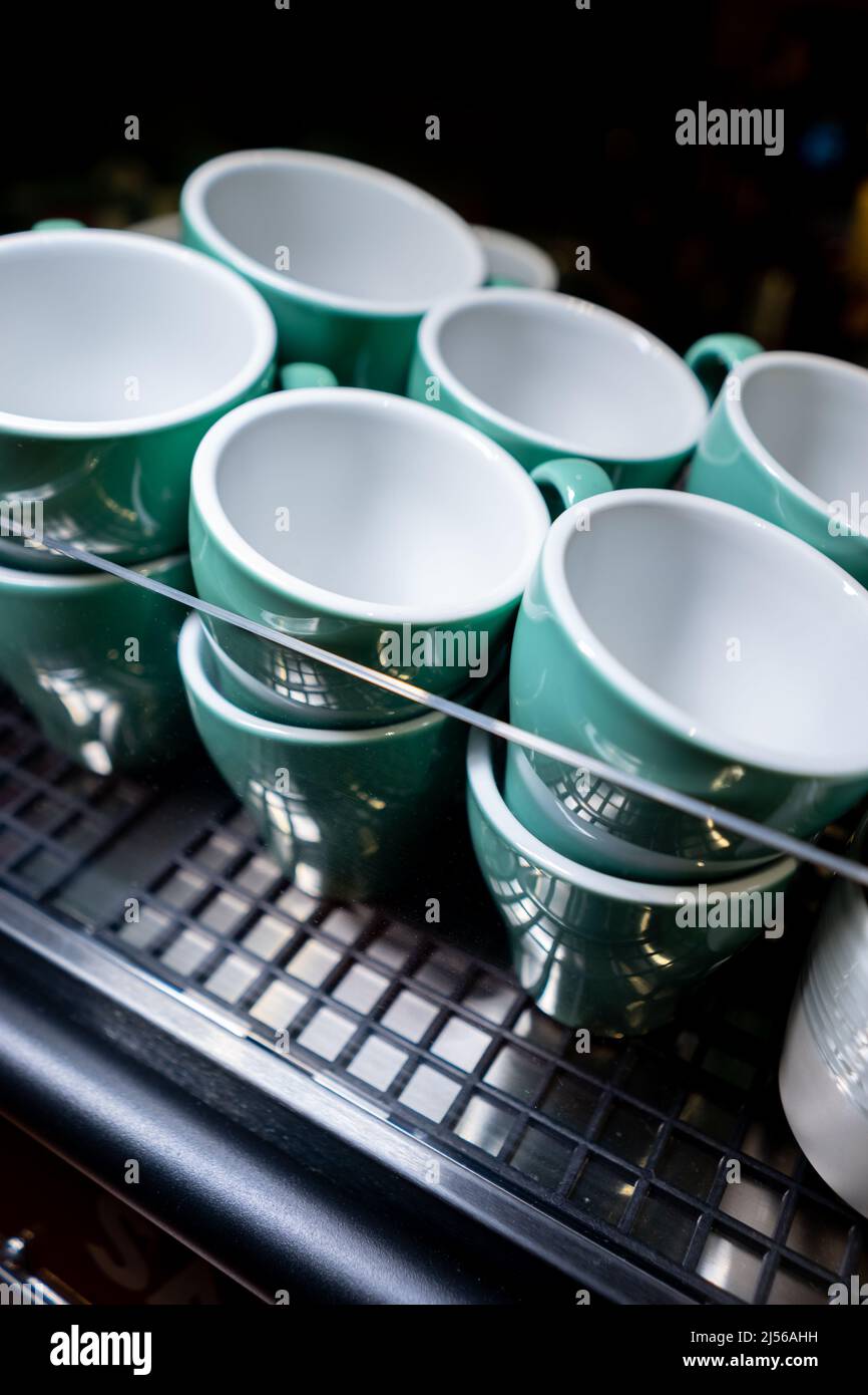 Set aus Keramikbechern oder Tassen, die auf einer professionellen Kaffeemaschine erhitzt werden Stockfoto