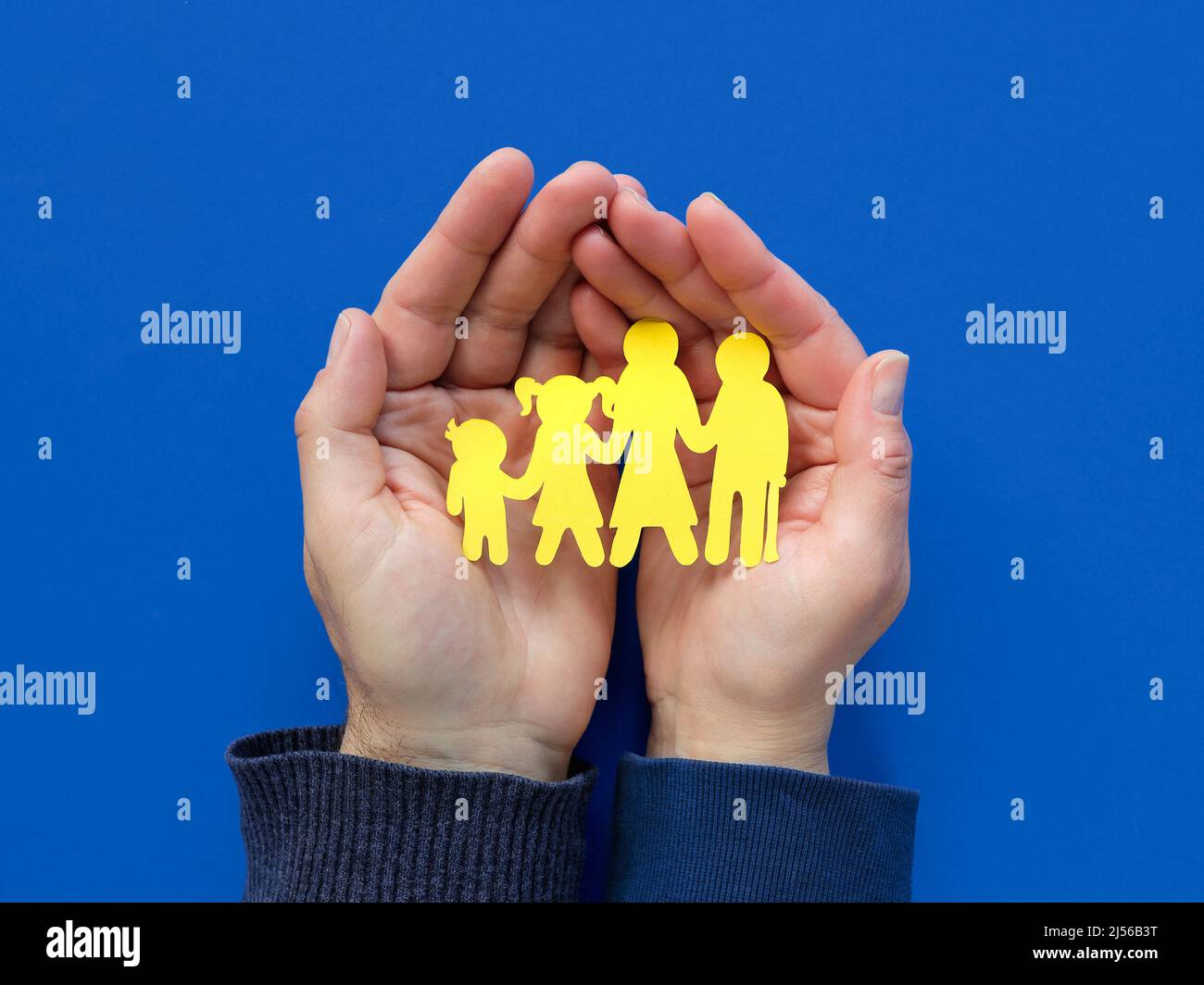 Helfende Hände, männlich und weiblich, mit gelber Papiersilhouette der ukrainischen Familie. Flach liegend, Draufsicht auf blauem Hintergrund. Stockfoto